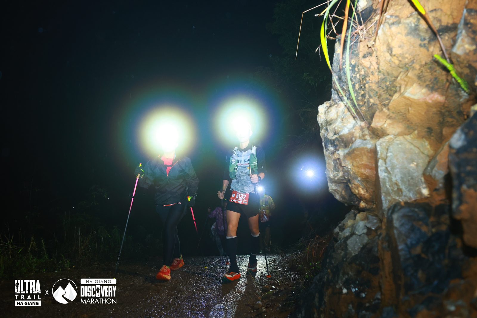 Hai runner chạy trail ban đêm với đèn pin trán trên địa hình đá